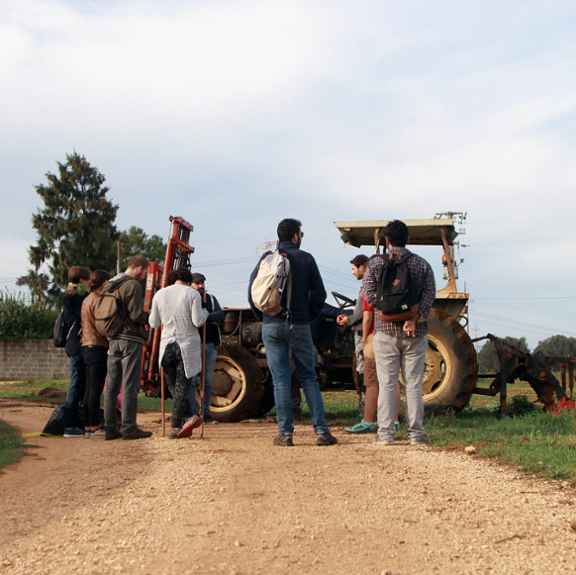 Een groep jongeren in gesprek met een boer op zijn land.